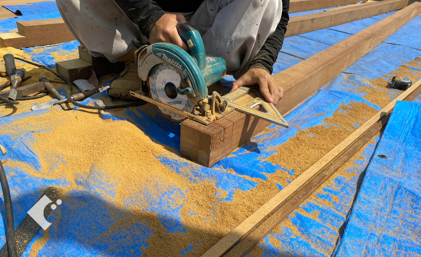 梁の一部を削るために丸ノコを使って材木を切る職人のパーゴラ設置作業