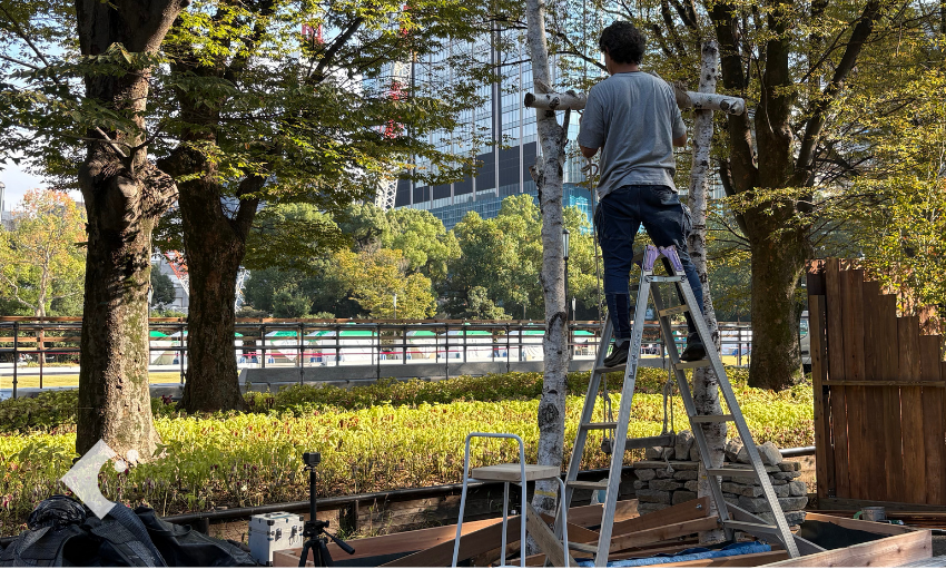 脚立に乗って白樺の支柱にブランコの横木を固定している施工1日目の様子